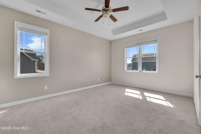 spare room featuring a raised ceiling, carpet flooring, baseboards, and visible vents