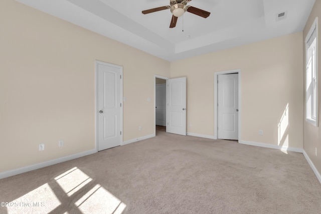 unfurnished bedroom with a tray ceiling, carpet flooring, baseboards, and visible vents