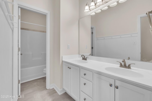 bathroom featuring double vanity, toilet, wood finished floors, and a sink