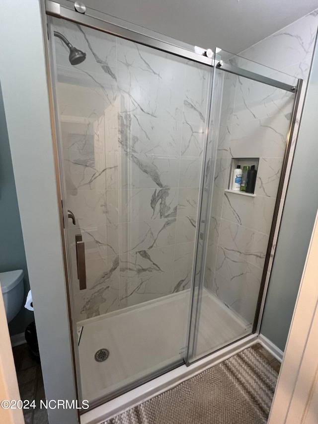 full bath with a marble finish shower and toilet