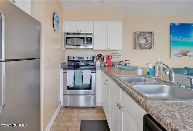 kitchen with stone finish floor, a sink, white cabinetry, stainless steel appliances, and baseboards