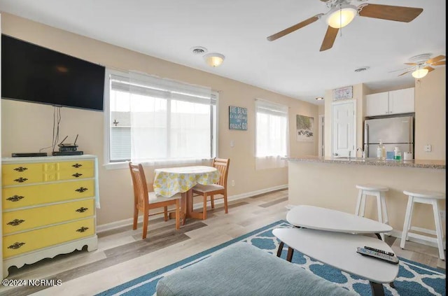 living area with visible vents, baseboards, light wood-type flooring, and a ceiling fan