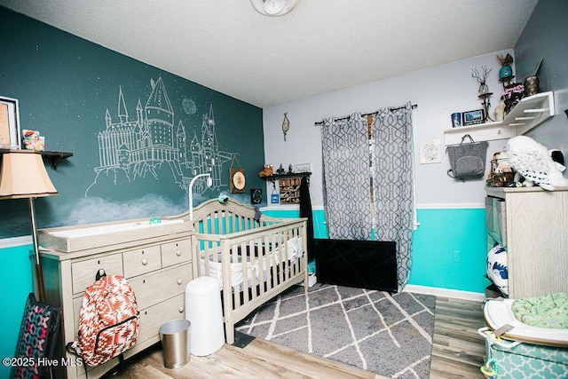 bedroom with baseboards, a nursery area, and wood finished floors