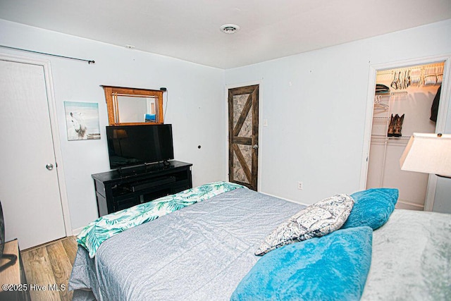 bedroom featuring a closet, visible vents, a walk in closet, and wood finished floors