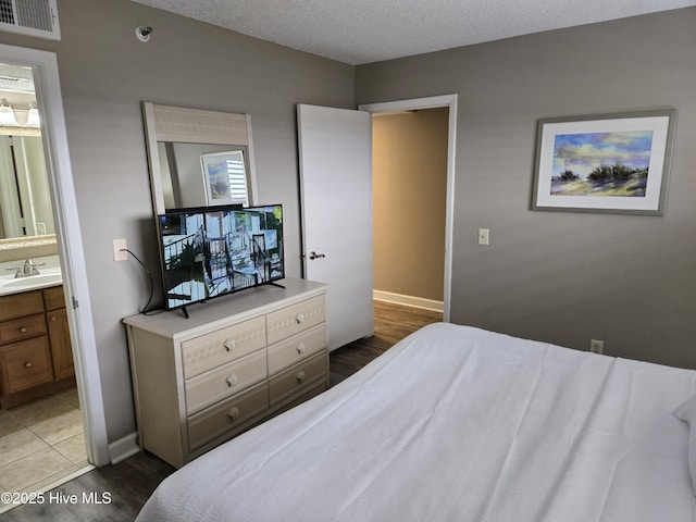 bedroom featuring visible vents, baseboards, wood finished floors, a textured ceiling, and a sink