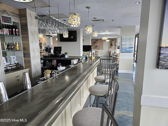 bar with visible vents, a drop ceiling, concrete flooring, a dry bar, and hanging light fixtures