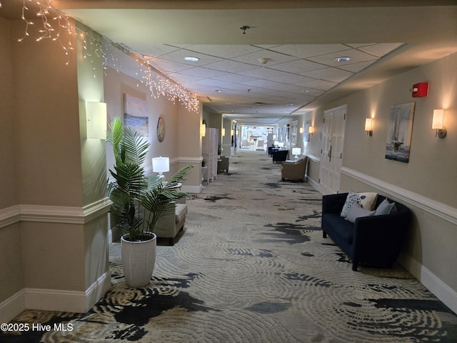 corridor with a paneled ceiling, baseboards, and carpet floors