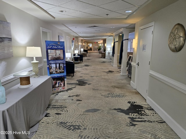 corridor featuring a paneled ceiling, carpet floors, and baseboards