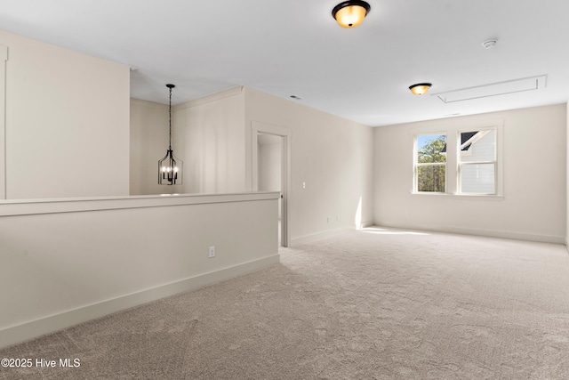 carpeted spare room featuring baseboards, an inviting chandelier, and attic access