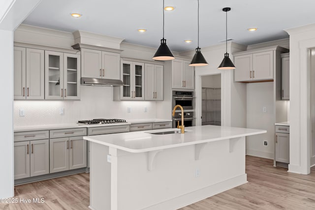 kitchen featuring light countertops, a center island with sink, under cabinet range hood, and stainless steel appliances