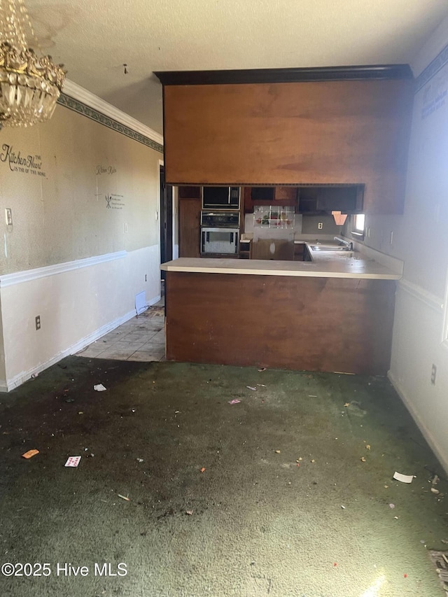 kitchen featuring wall oven, ornamental molding, a peninsula, a textured ceiling, and a sink