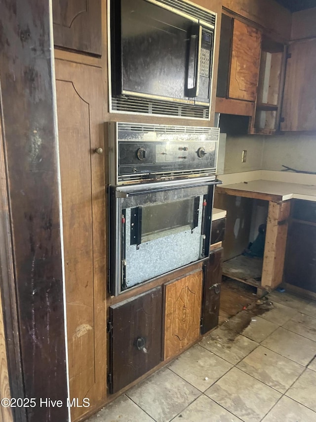 kitchen featuring light tile patterned flooring, wall oven, brown cabinetry, and black microwave