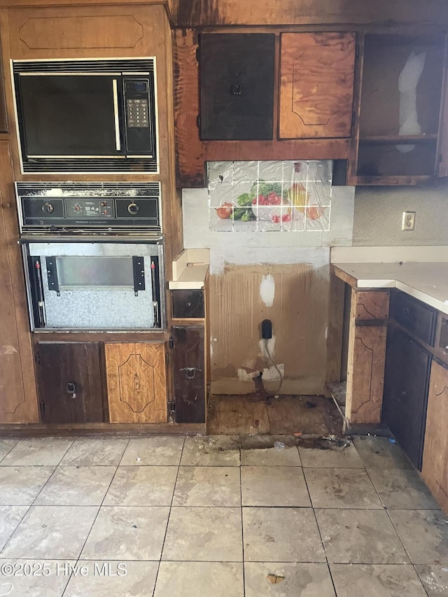 kitchen featuring light tile patterned floors, light countertops, oven, and black microwave