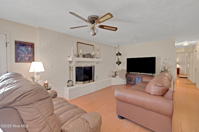 living room featuring a fireplace with raised hearth, a textured ceiling, a ceiling fan, and wood finished floors