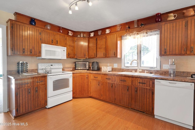 kitchen with light countertops, light wood-type flooring, brown cabinetry, white appliances, and a sink