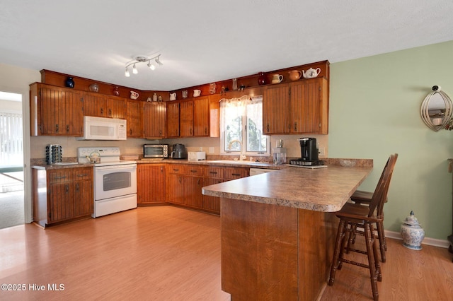 kitchen featuring brown cabinets, white appliances, a peninsula, and a sink