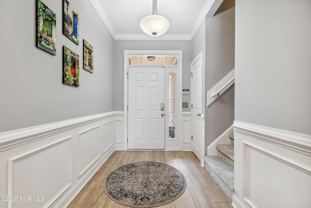 entryway featuring light wood finished floors, stairs, ornamental molding, wainscoting, and a decorative wall