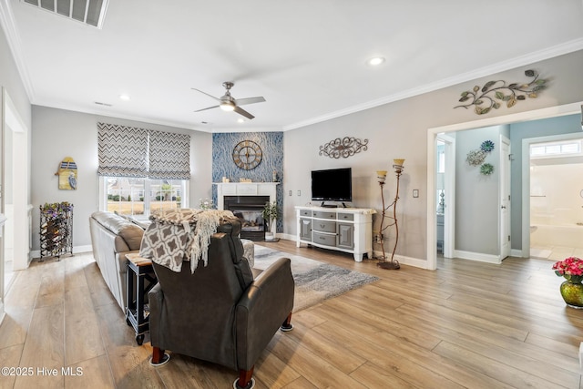 living area with light wood finished floors, visible vents, a fireplace, and a ceiling fan