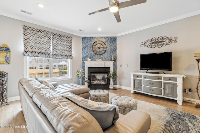 living area with wood finished floors, a ceiling fan, baseboards, and ornamental molding