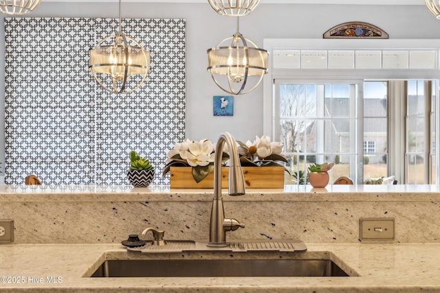 kitchen with a notable chandelier, light stone countertops, pendant lighting, and a sink