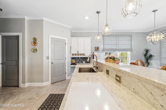 kitchen featuring light stone counters, a sink, white cabinets, crown molding, and backsplash