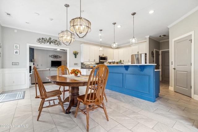 dining room featuring visible vents, crown molding, a chandelier, a wainscoted wall, and a decorative wall