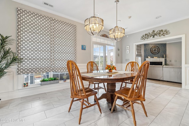 dining area featuring a notable chandelier, visible vents, a tiled fireplace, and crown molding