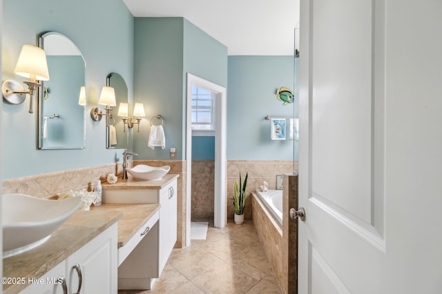 full bath featuring a relaxing tiled tub, double vanity, tile patterned floors, tile walls, and a sink