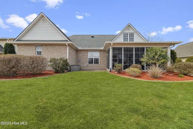 rear view of house with a yard, brick siding, roof with shingles, and a sunroom