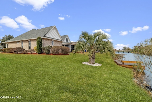 view of side of property featuring brick siding, a lawn, and a water view