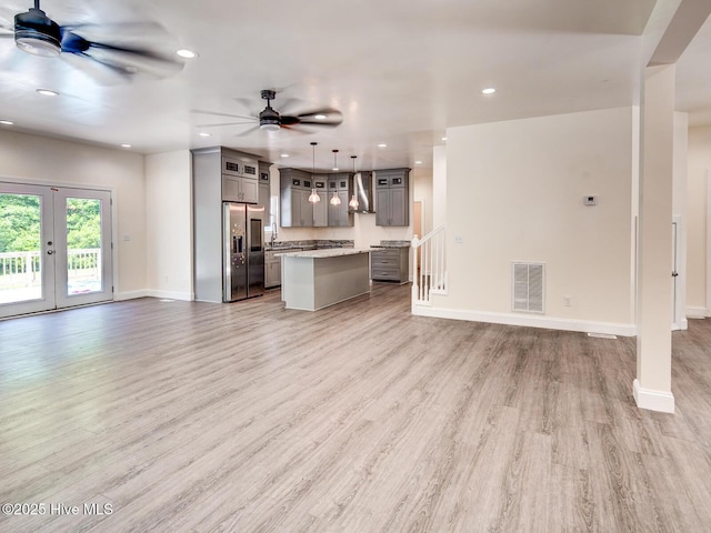 kitchen featuring open floor plan, gray cabinetry, wall chimney exhaust hood, and visible vents