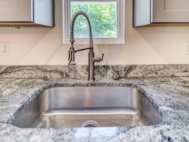 room details with gray cabinets, light stone countertops, and a sink