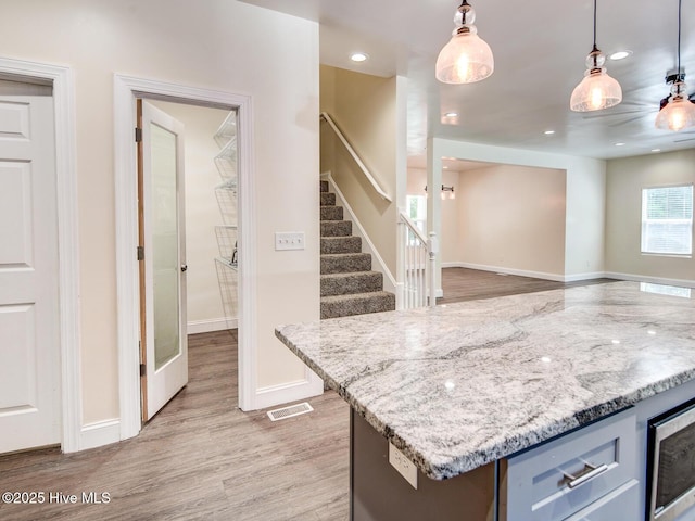 kitchen with light stone counters, visible vents, baseboards, light wood-style flooring, and hanging light fixtures