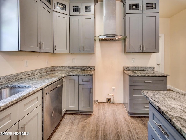 kitchen with light stone counters, light wood finished floors, gray cabinets, dishwasher, and wall chimney range hood