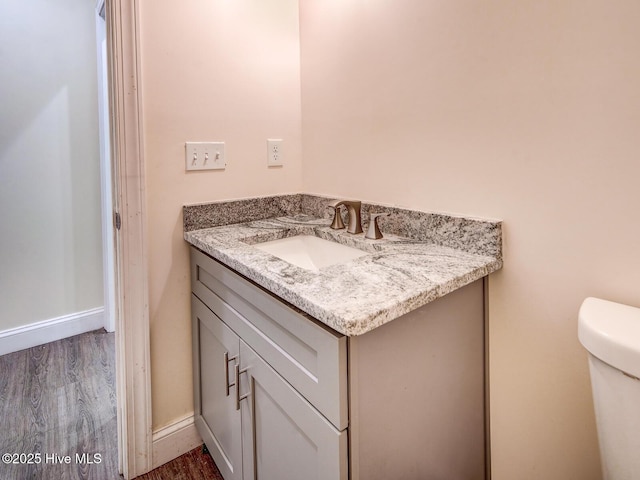 bathroom with toilet, vanity, baseboards, and wood finished floors