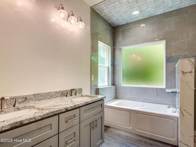 full bath featuring a bath, double vanity, wood finished floors, and a sink