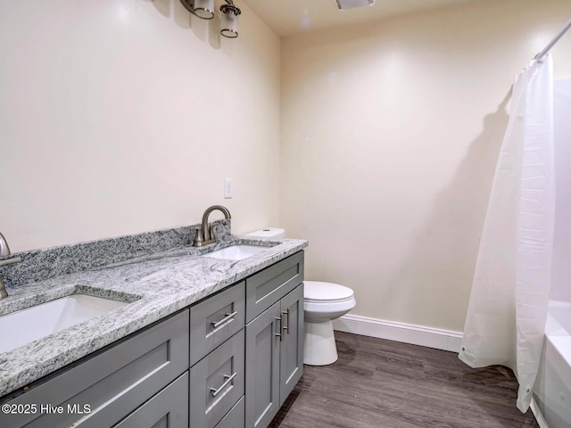 bathroom with toilet, wood finished floors, baseboards, and a sink