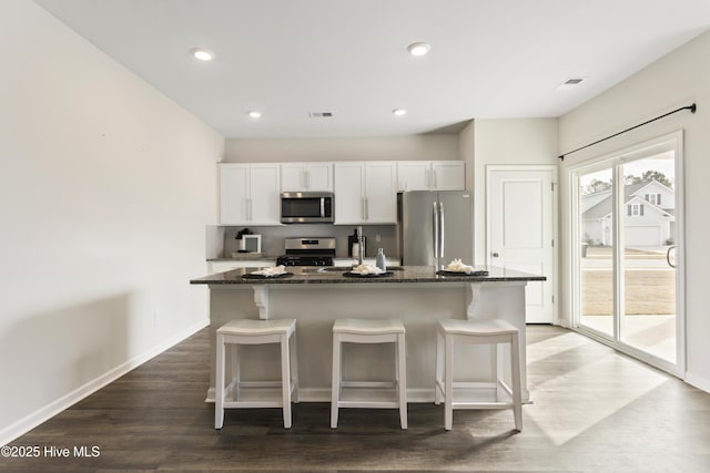 kitchen with a breakfast bar, dark stone counters, a center island with sink, and stainless steel appliances