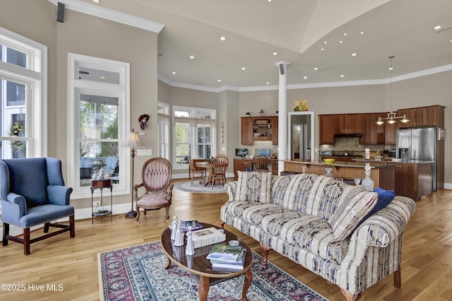 living area featuring light wood-type flooring, baseboards, a high ceiling, and crown molding