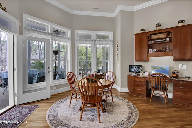 dining space featuring visible vents, baseboards, light wood finished floors, ornamental molding, and built in desk