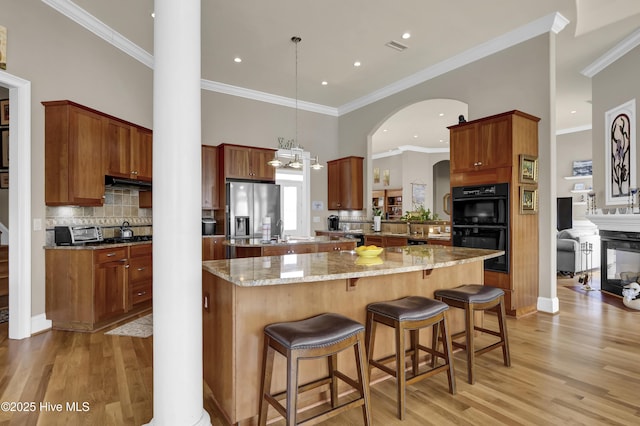 kitchen featuring dobule oven black, stainless steel refrigerator with ice dispenser, under cabinet range hood, backsplash, and a center island