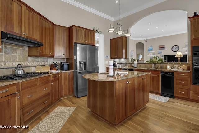 kitchen featuring under cabinet range hood, light stone counters, stainless steel refrigerator with ice dispenser, arched walkways, and gas stovetop