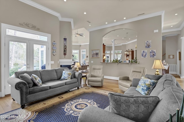 living room featuring light wood-type flooring, visible vents, arched walkways, crown molding, and ceiling fan