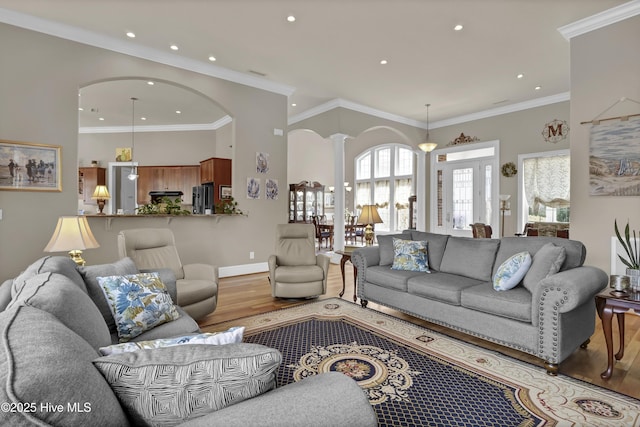 living area with baseboards, ornamental molding, decorative columns, wood finished floors, and arched walkways