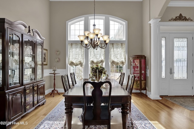 dining space with light wood-style flooring, a notable chandelier, a towering ceiling, and decorative columns