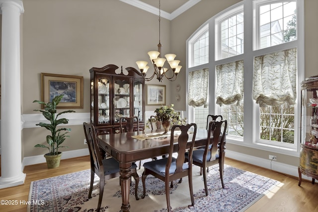 dining space featuring decorative columns, light wood-style floors, an inviting chandelier, and crown molding