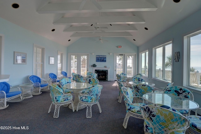 carpeted dining space featuring beam ceiling, high vaulted ceiling, a ceiling fan, and a premium fireplace