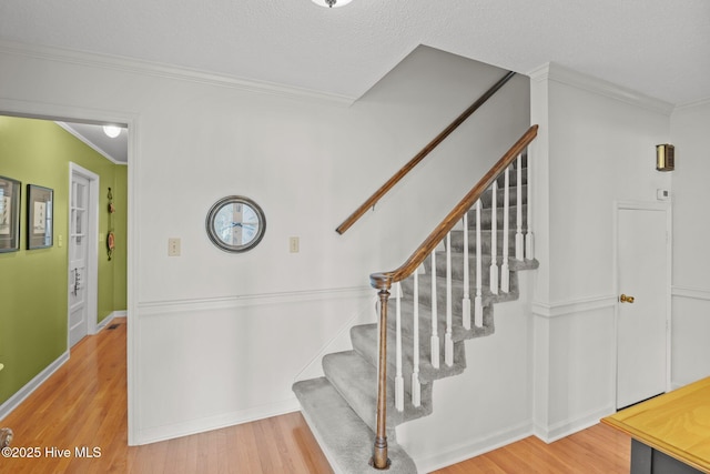 staircase with baseboards, a textured ceiling, wood finished floors, and crown molding