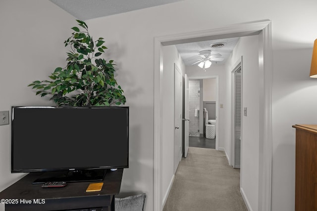 corridor featuring visible vents, baseboards, light colored carpet, and a textured ceiling