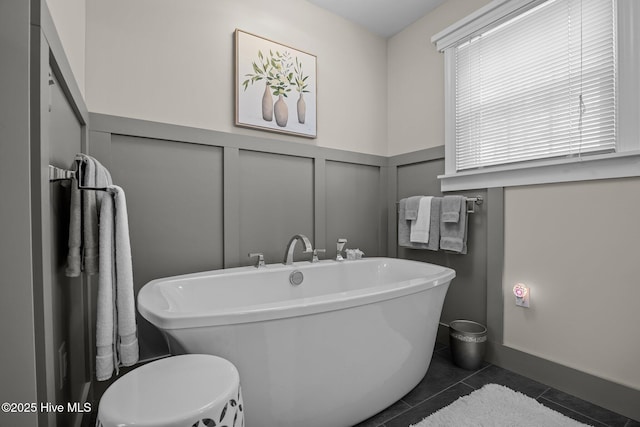 bathroom with tile patterned flooring, a decorative wall, a freestanding bath, and a wainscoted wall